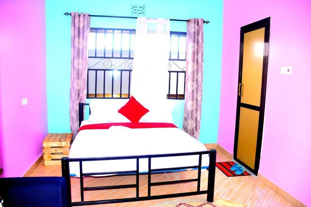 A room with a bed, a window with metal bars, a door, and a small wooden stool.