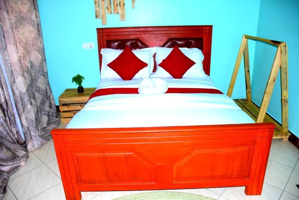 A bed with a red headboard and white bedding, a small bedside table with a plant, and a wooden frame against the wall.
