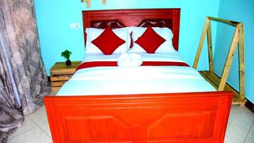 A bed with a red headboard and white bedding, a small bedside table with a plant, and a wooden frame against the wall.