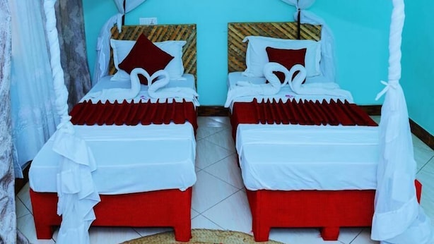 A room with two beds, each with a red base and white bedding, under a white canopy. - Safari Park House (Arusha)
