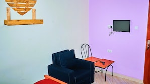 A room with a wooden heart decoration, a black sofa, a small table, a TV, and a chair. - Safari Park House (Arusha)