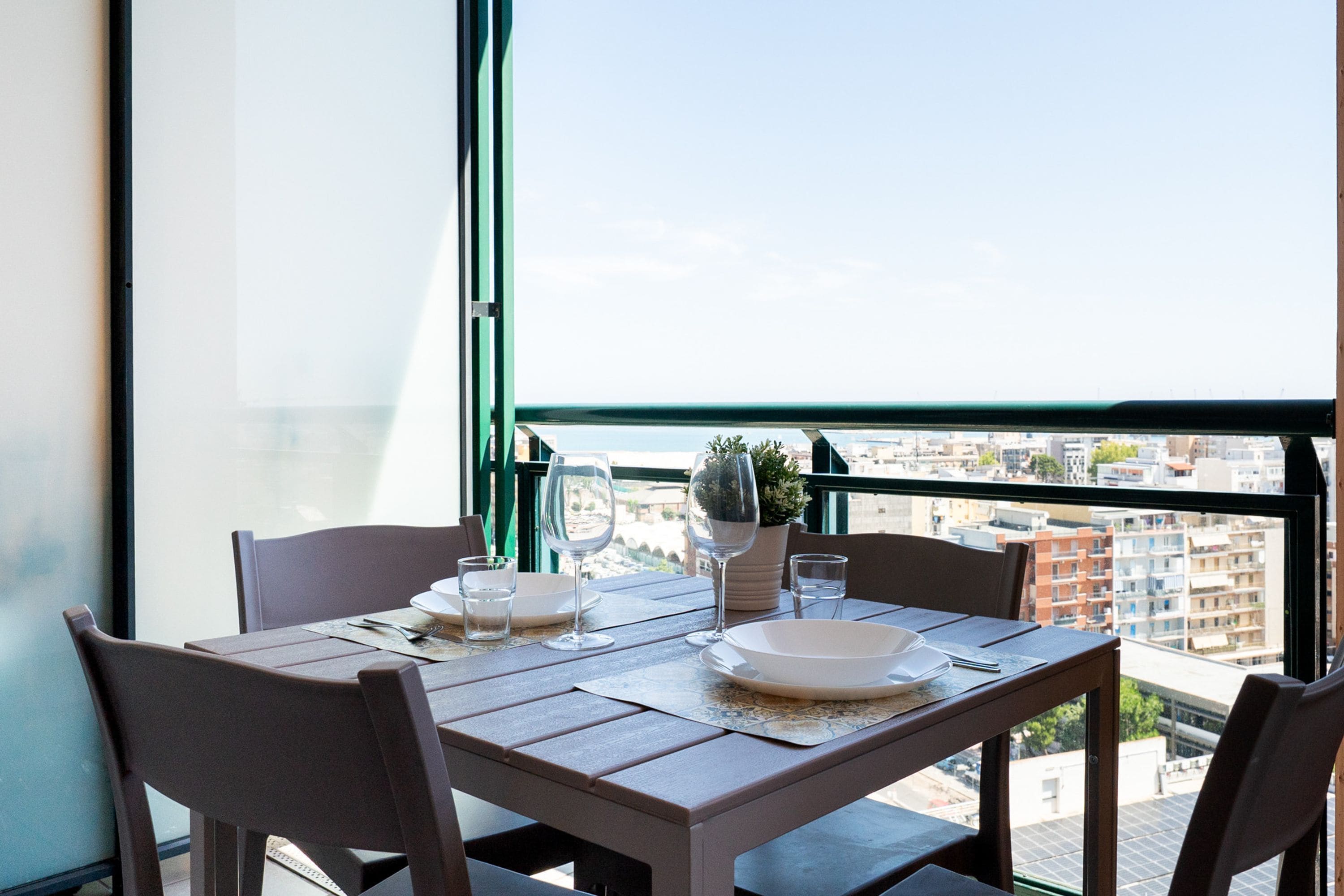 A dining table with chairs, a potted plant, and a view of the cityscape through a balcony railing.