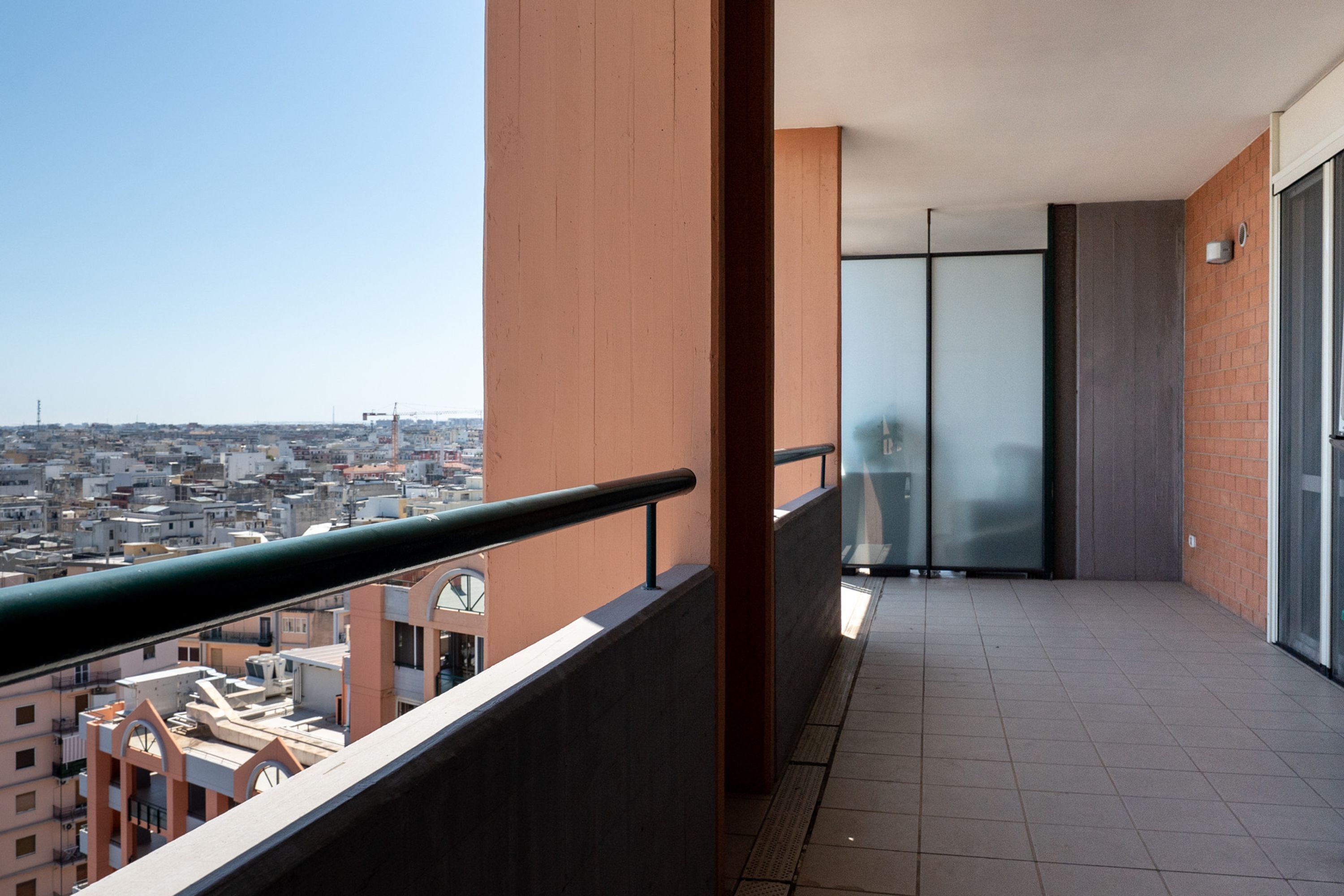 Un balcón con vista a la ciudad, una puerta de cristal y piso de baldosas.