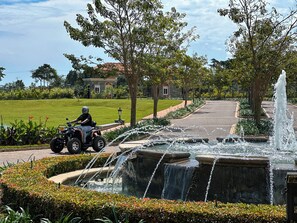A paved pathway with a water feature and a person riding an ATV. - Avellino Lakeside Escape (Entebbe)