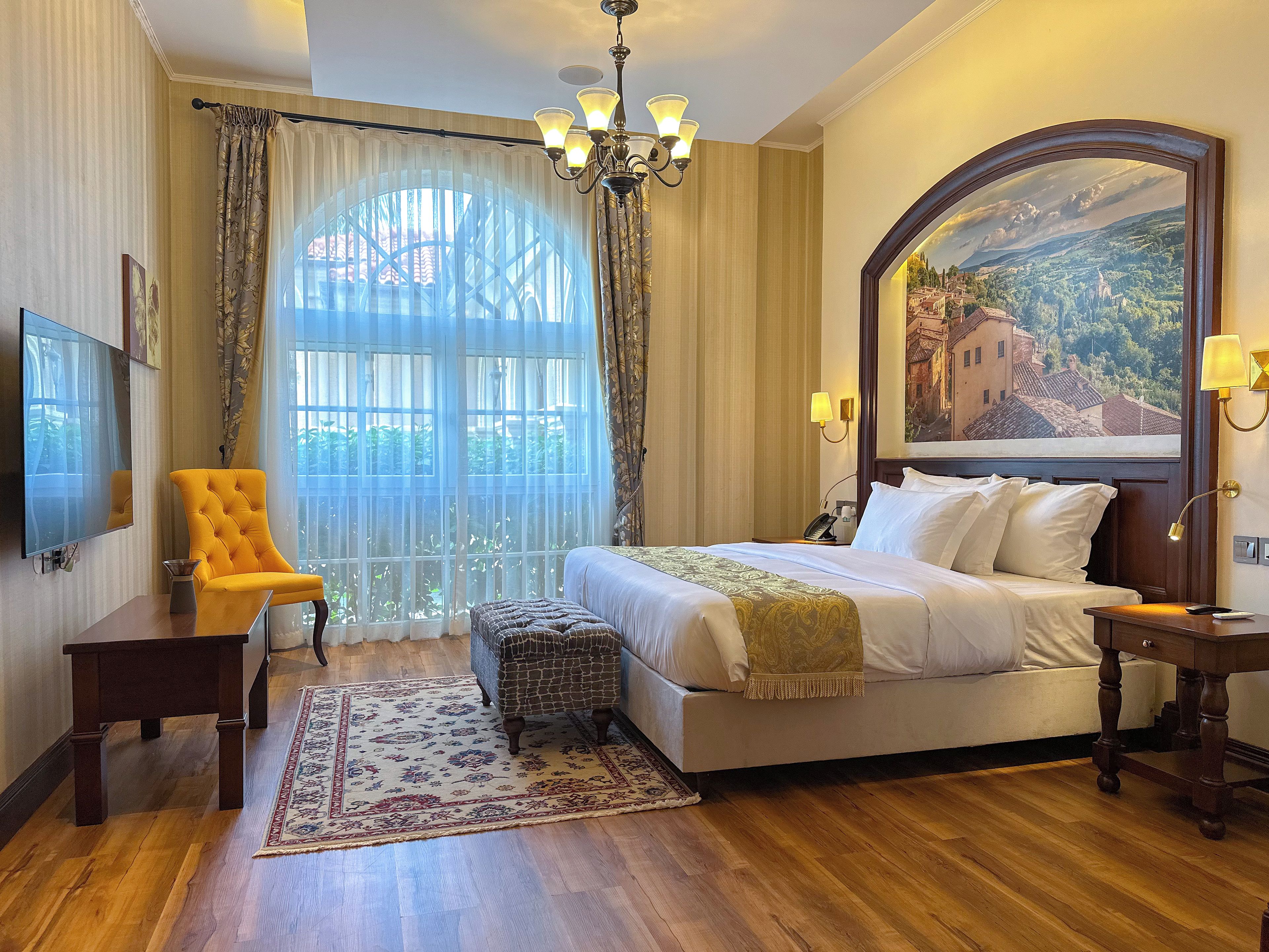 A hotel room with a large bed, a television, a chair, a desk, and a view of a landscape through a window.