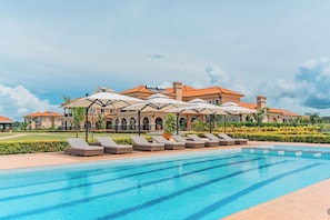A swimming pool with lounge chairs and umbrellas, surrounded by a landscaped garden and a large building with a tiled roof. - Avellino Lakeside Escape (Entebbe)