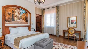 A hotel room with a large bed, a desk, a chair, a mirror, and a painting of a street scene. - Avellino Lakeside Escape (Entebbe)