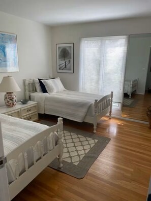 A bedroom with two beds, a nightstand, a lamp, and a window with blinds. - 99 steps to the beach! Charming 3 bedroom house! (Amagansett)