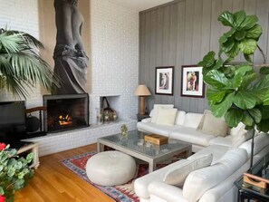 Ein Wohnzimmer mit Kamin, weißem Sofa und einer großen Zimmerpflanze.