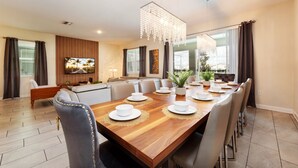 A dining area with a wooden table set for six, a chandelier, and a large window with curtains. - 8886-CabotCliffs (Kissimmee)