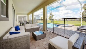 A covered outdoor area with wicker furniture, a glass coffee table, and a view of a swimming pool. - 8886-CabotCliffs (Kissimmee)