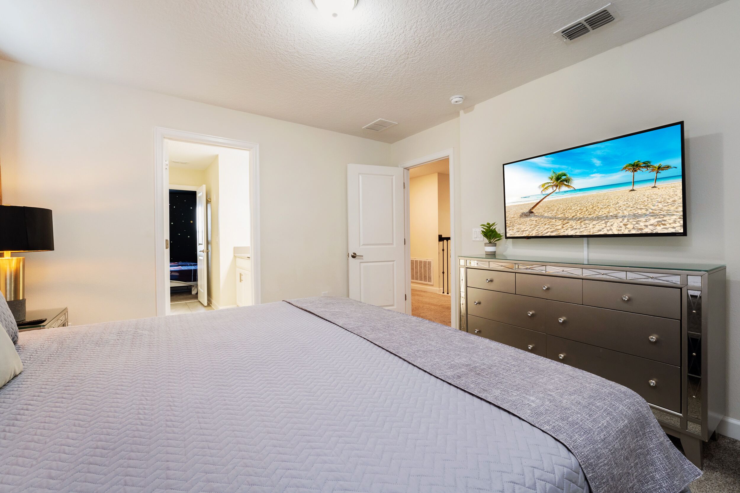 A bedroom with a bed, a dresser, a television displaying a beach scene, and a door leading to another room.