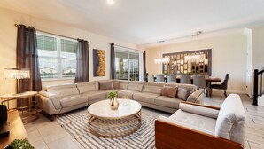 A modern living room with a sectional sofa, a round coffee table, and a dining area with a chandelier. - 8886-CabotCliffs (Kissimmee)