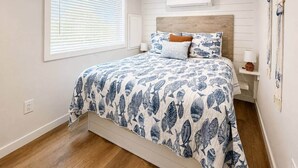 Una camera da letto con un letto, comodini, una finestra con tende e condizionatore d'aria a muro.
