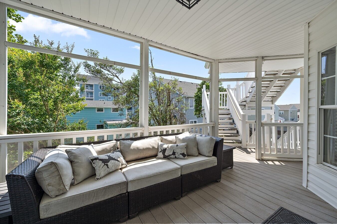 A covered porch with a sofa and railing, overlooking a residential area.