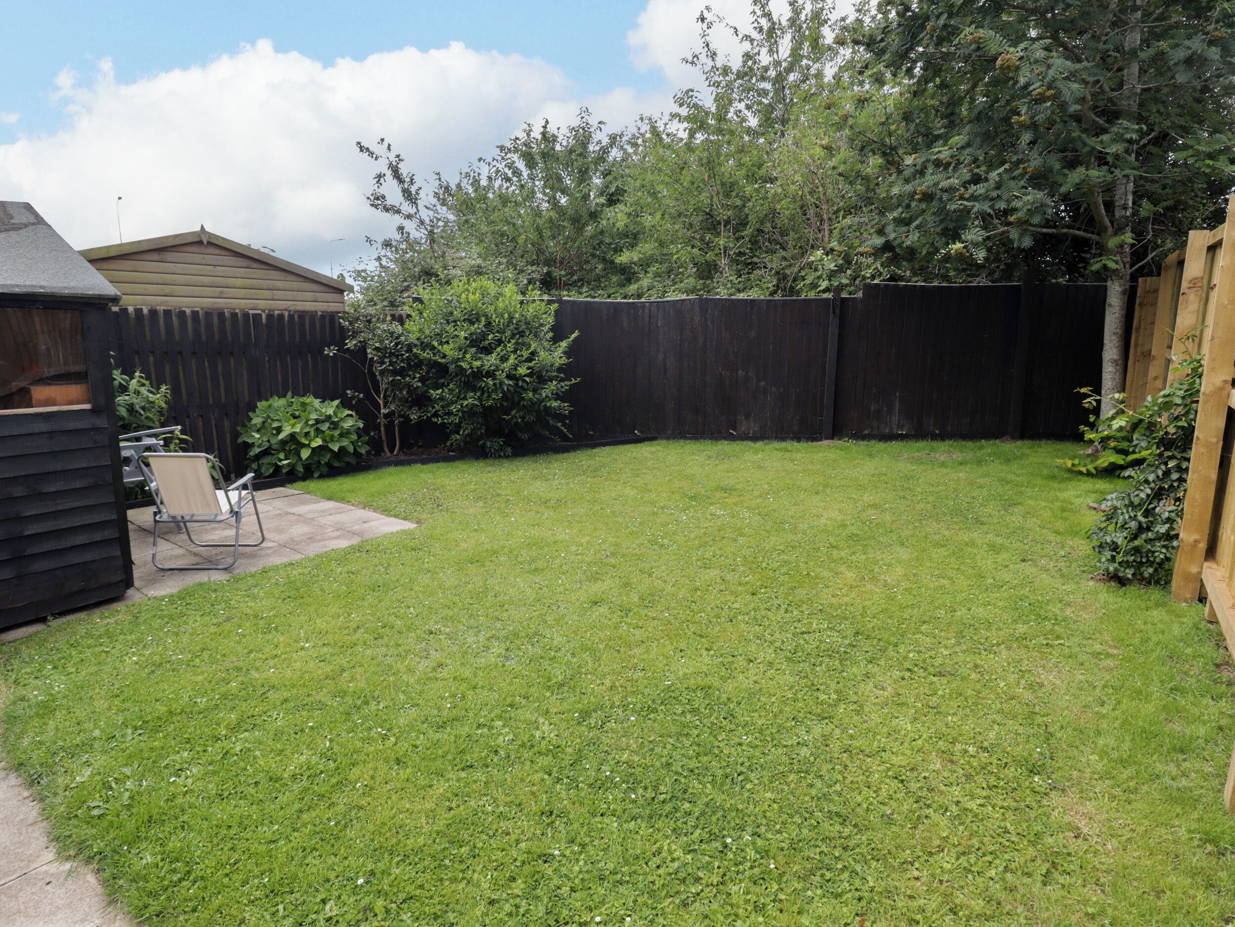 A backyard with a wooden fence, a lawn, and a patio area with a chair.