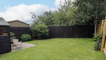A backyard with a wooden fence, a lawn, and a patio area with a chair.