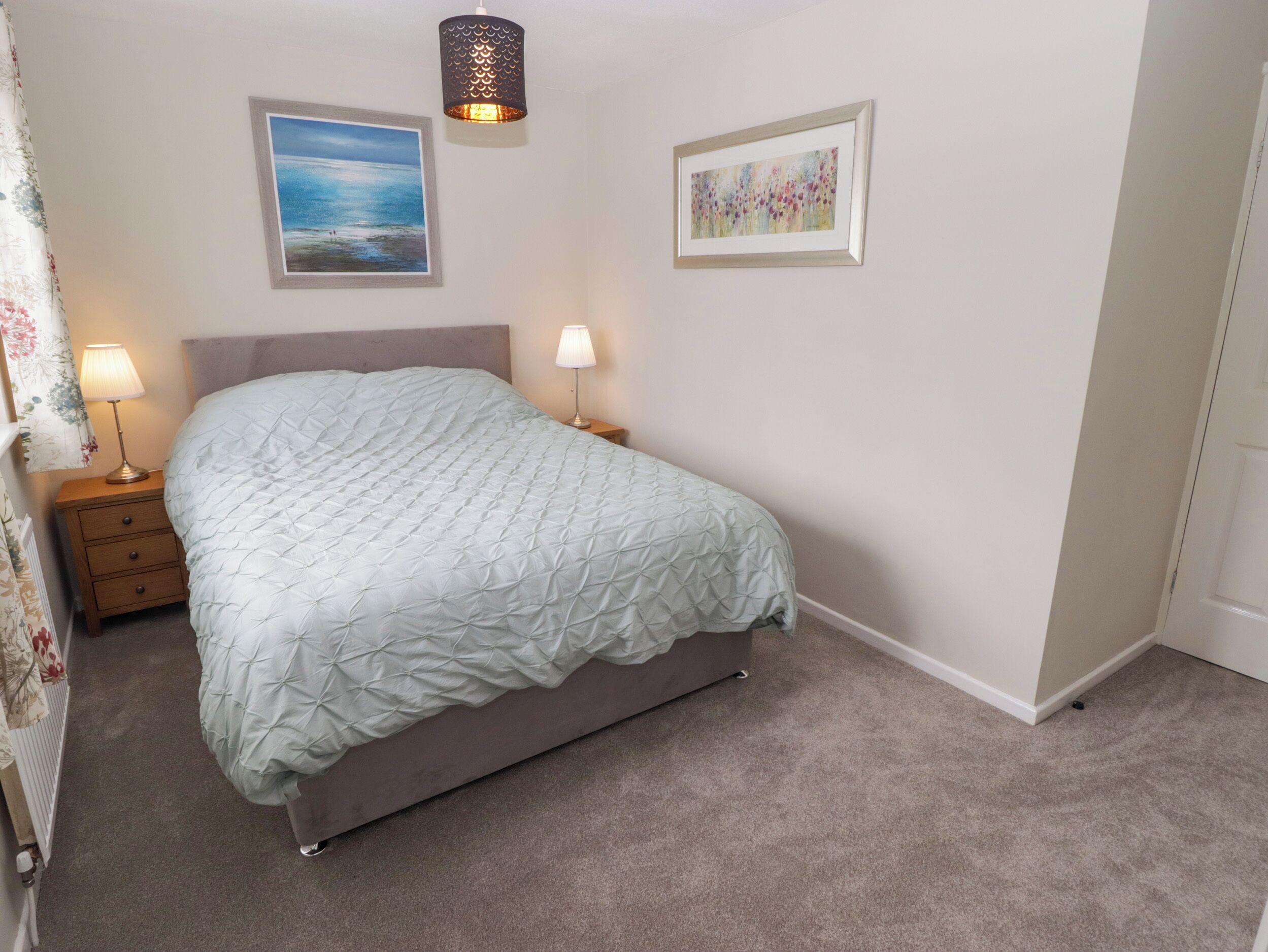 Un dormitorio con cama, dos lámparas de noche, un cuadro enmarcado y una lámpara de pared.