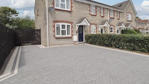 A residential house with a paved driveway, brick exterior, and multiple windows.