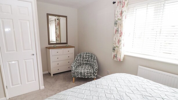A bedroom with a bed, a dresser, a chair, a mirror, and a window with curtains.