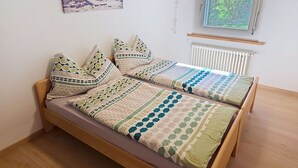 En enkelt seng med træstel, et tæppe med geometriske mønstre og en radiator på væggen.