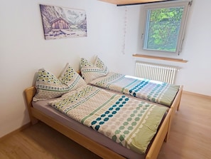 Uma cama de solteiro com estrutura de madeira, um edredom com padrões geométricos e um radiador fixado na parede.