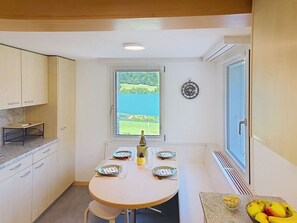 Uma cozinha compacta com mesa de jantar para quatro pessoas, janela com vista para área verde e relógio de parede.