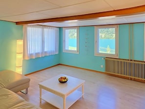 Quarto com mesa branca, sofá e duas janelas com cortinas.