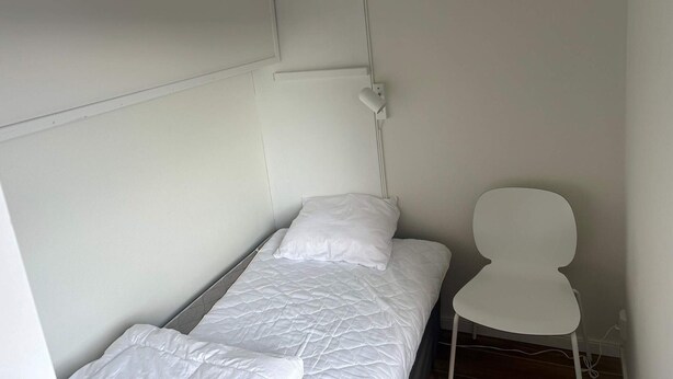A small, single-bed room with a white headboard, a bedside lamp, and a white chair. - 5 Star Holiday Home in Uddevalla (Uddevalla)