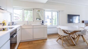 Eine moderne Küche mit weißen Schränken, Holzboden, einem Esstisch mit Stühlen und einem großen Fenster, das natürliches Licht hereinlässt.