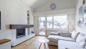 Ein modernes Wohnzimmer mit Kamin, einer Couch, einem Couchtisch und einem großen Fenster mit Blick auf Gebäude.