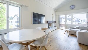 Ein modernes Wohnzimmer mit einem runden Esstisch, weißen Stühlen, einem Flachbildfernseher und einem Sofa.