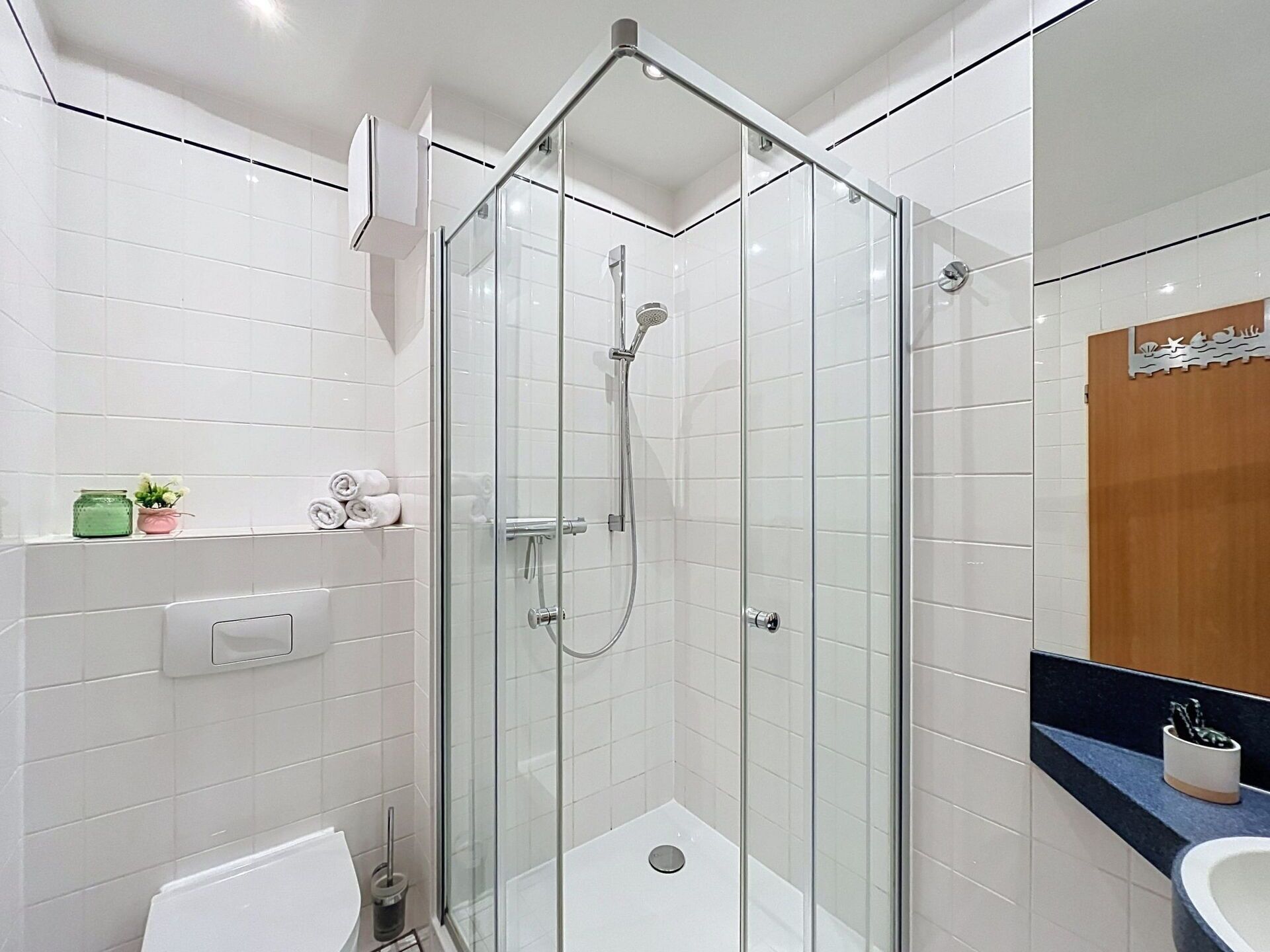 Ein modernes Badezimmer mit einer gläsernen Dusche, weißen Fliesenwänden, einer Toilette und einem Waschbecken mit blauer Arbeitsplatte.