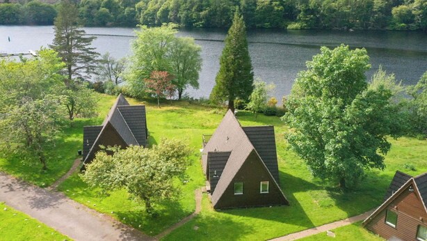 A lakeside property with three triangular-roof cottages, a paved driveway, and a forested backdrop. - Stunning private villa for 6 people with WIFI, TV, terrace, pets allowed and panoramic view (Invergarry)