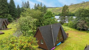 A row of triangular-roofed cabins with a grassy yard and a lake in the background. - Stunning private villa for 6 people with WIFI, TV, terrace, pets allowed and panoramic view (Invergarry)