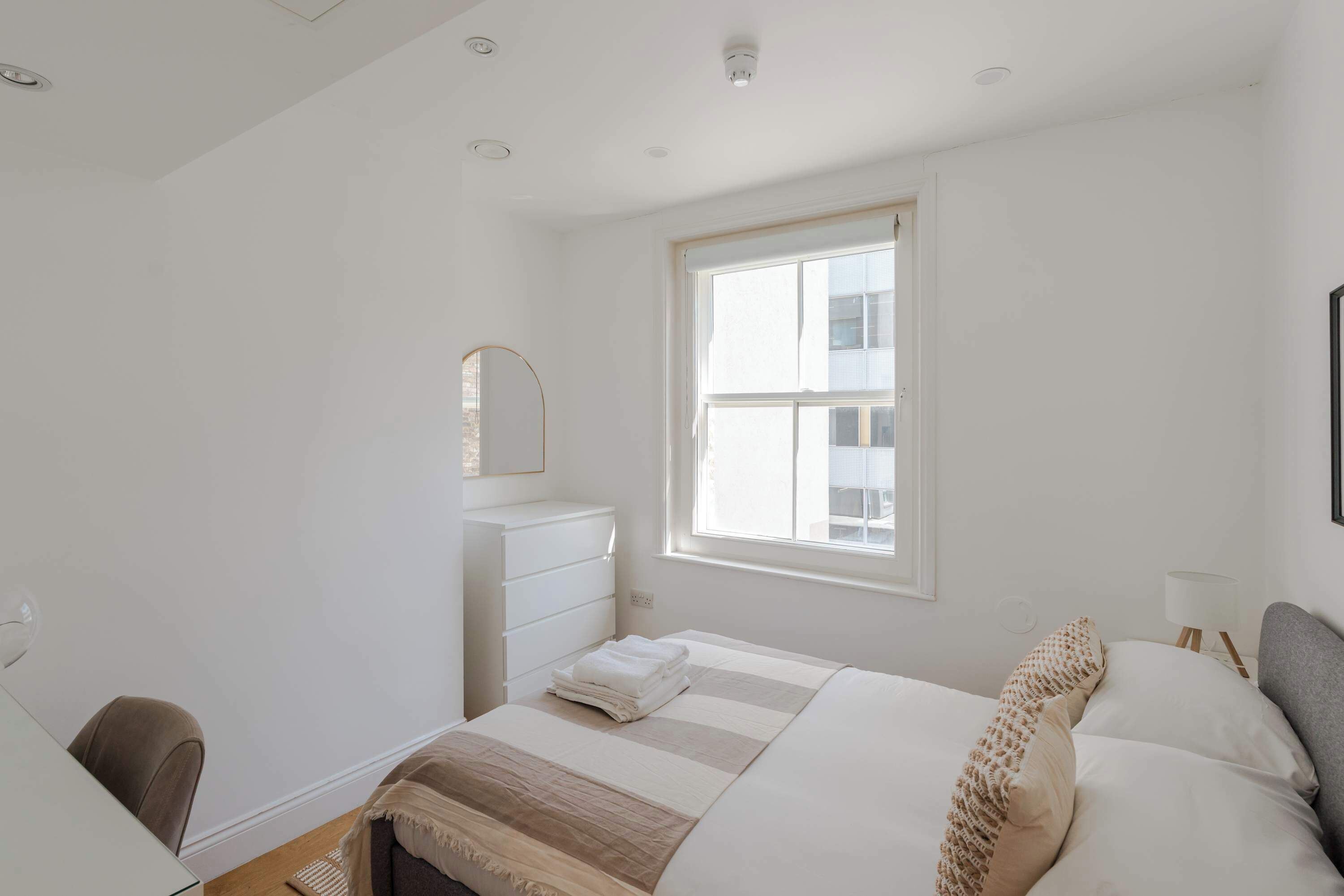 Een slaapkamer met een bed, een dressoir, een raam en een bureau.