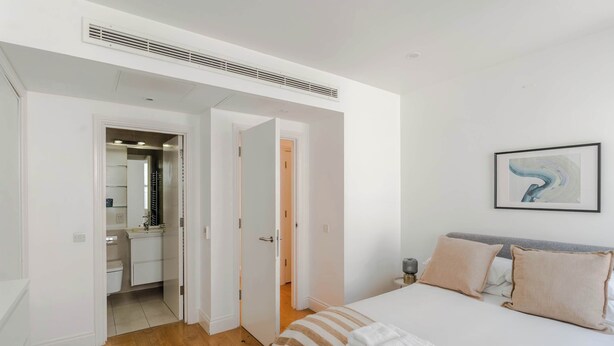 A bedroom with a bed, a bedside table, a nightstand, a framed picture on the wall, and a bathroom visible through an open door. - 3-bed Flat Near Oxford Circus Sleeps 6 AC (London)