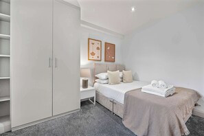 A bedroom with a bed, bedside tables, a wardrobe, and two framed pictures on the wall. - Comfy 1-bed in Soho, Steps From Carnaby Street (London)