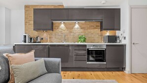 A modern kitchen with dark cabinets, a brick backsplash, and built-in appliances. - Comfy 1-bed in Soho, Steps From Carnaby Street (London)