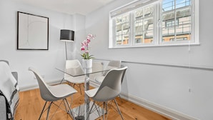 A modern dining area with a glass table and white chairs, a potted orchid, and a framed abstract artwork on the wall. - Comfy 1-bed in Soho, Steps From Carnaby Street (London)
