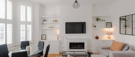 Uma sala de estar moderna com lareira, TV de tela plana e área de estar com mesa de vidro e cadeiras.