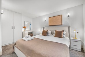 Une chambre d’hôtel moderne avec un grand lit, une table de chevet avec une lampe, une armoire et un miroir.