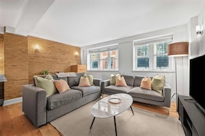 A modern living room with two grey sofas, a glass coffee table, and a brick accent wall. - Premium 1-bed Apartment in Soho, Near Carnaby St (London)
