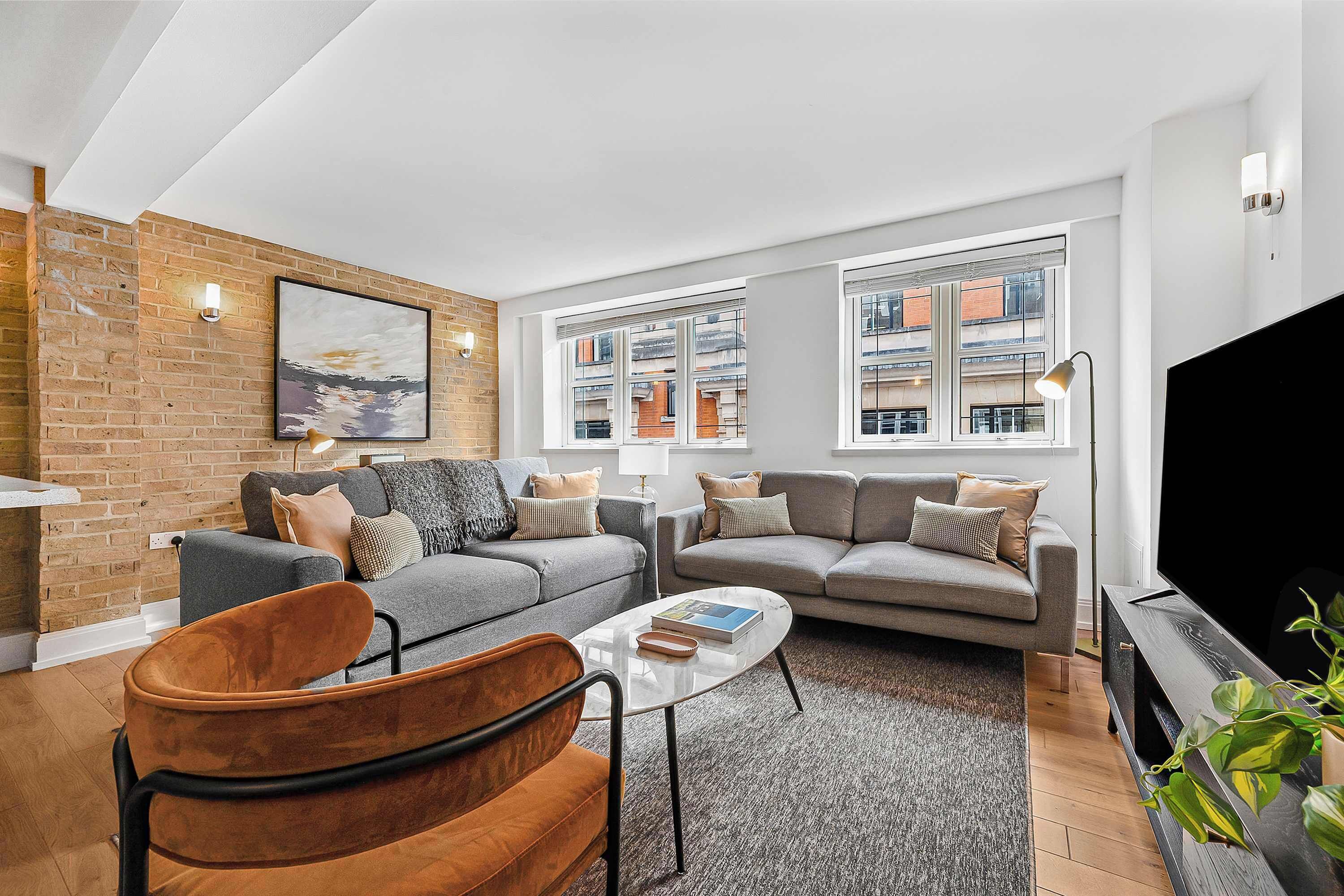A modern living room with two sofas, a coffee table, a TV, and a brick wall.