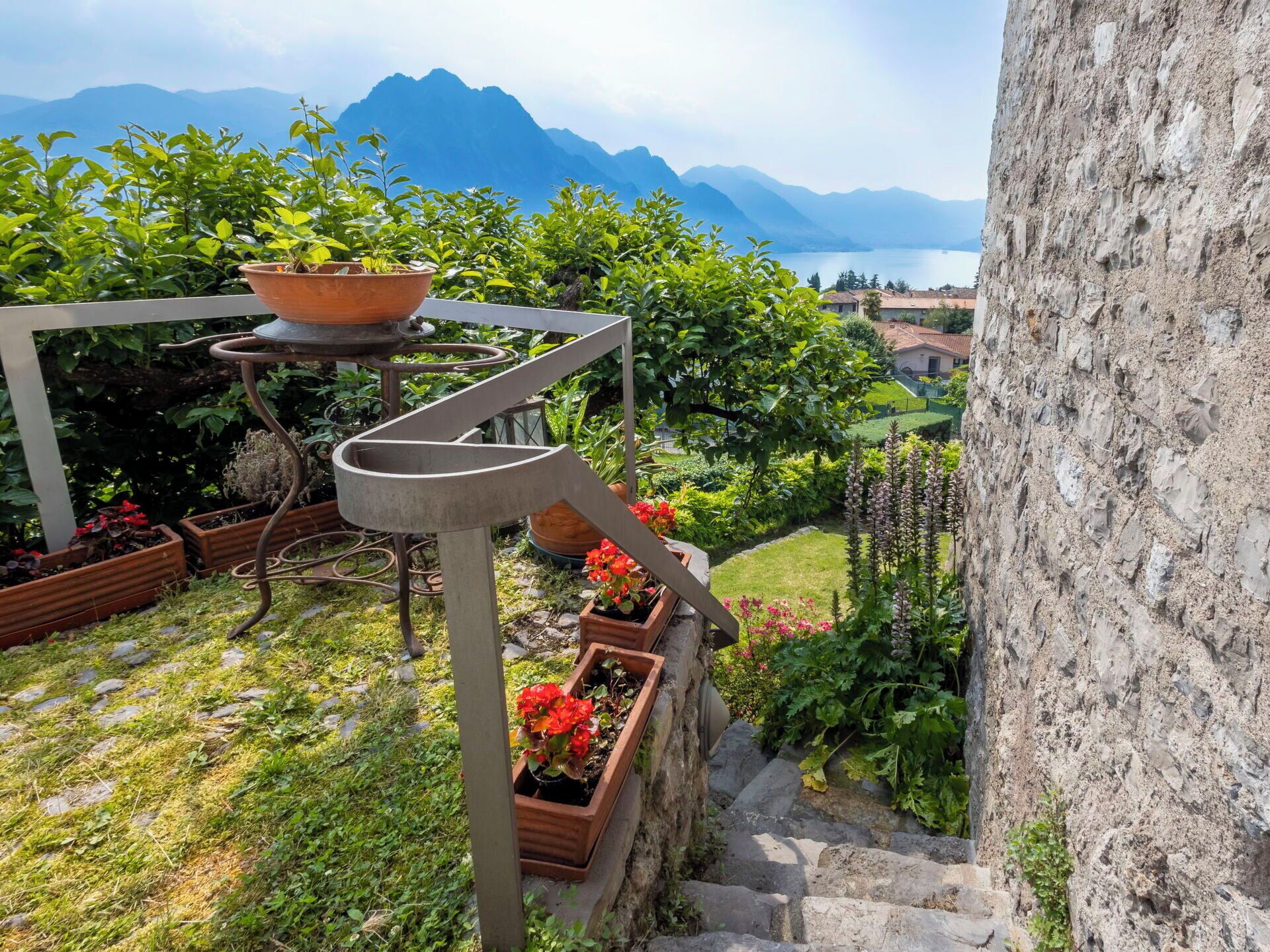 Ein Garten mit Blumentöpfen, einer Metall-Wendeltreppe und Blick auf Berge und einen See.