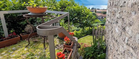 Ein Garten mit Blumentöpfen, einer Metall-Wendeltreppe und Blick auf Berge und einen See.