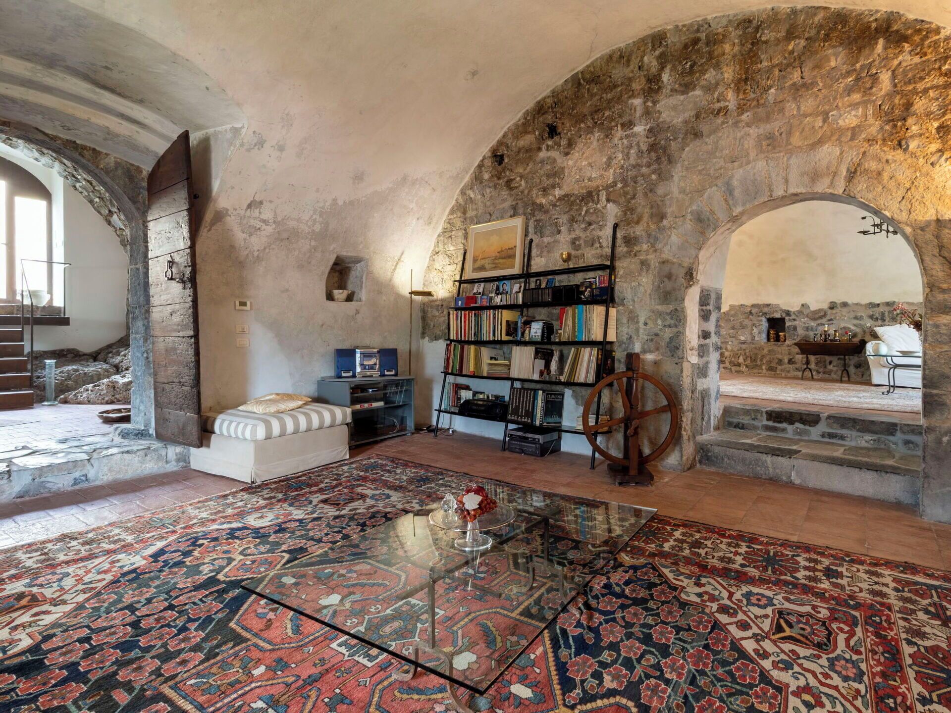 Ein Zimmer mit Steinwand, Bücherregal, Bett und Glastisch.