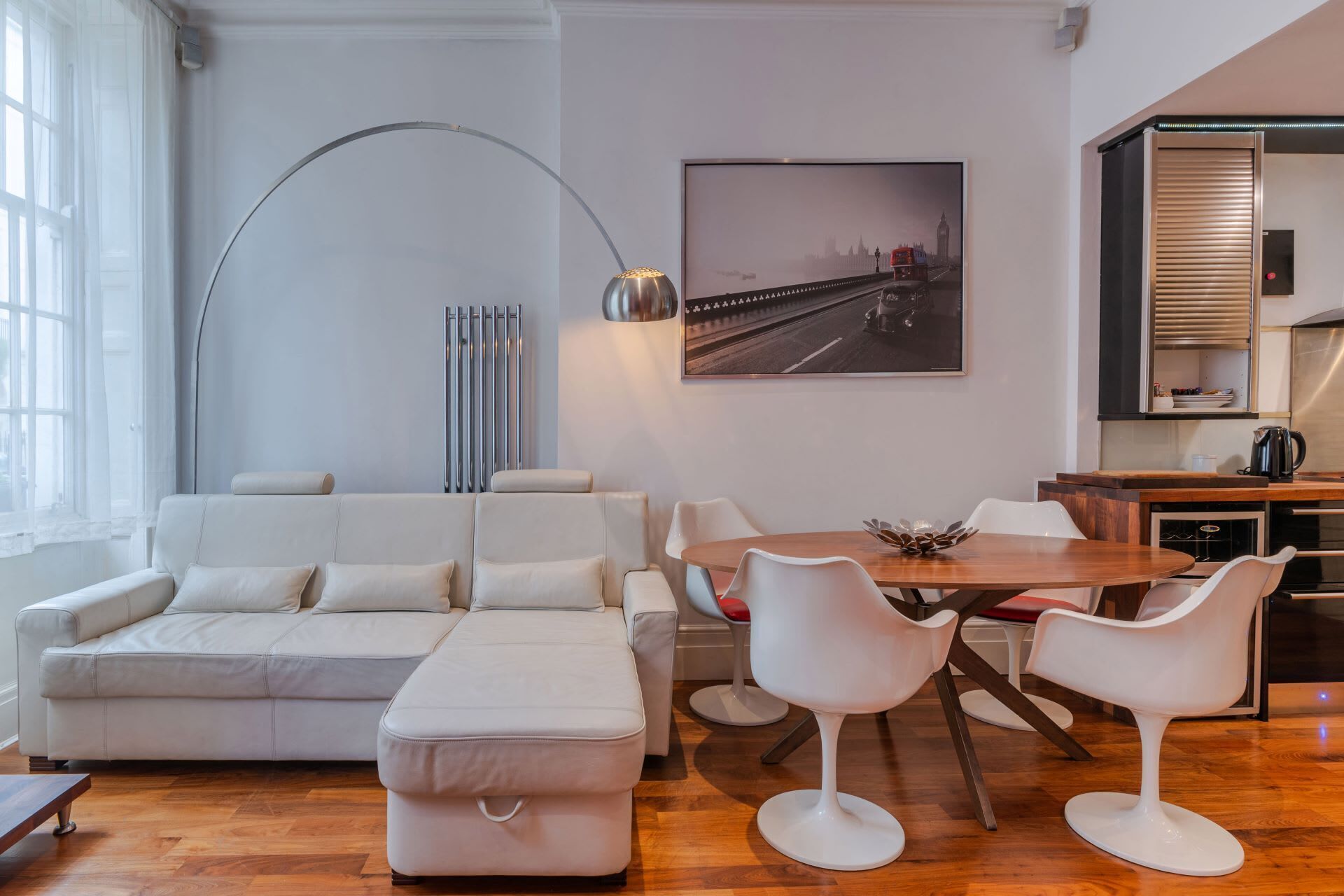 A modern living room with a sofa, ottoman, and a dining area with chairs and a table.