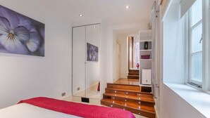 Ein Schlafzimmer mit einem Bett, einer roten Decke, einem Blumenbild, einem Kleiderschrank, einer Treppe und einem Fenster.