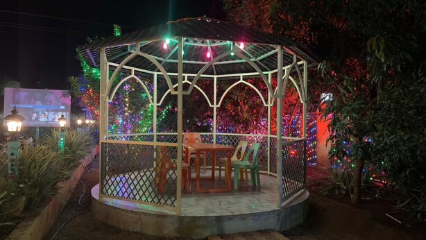 A gazebo with a table and chairs, surrounded by plants and colorful lights.